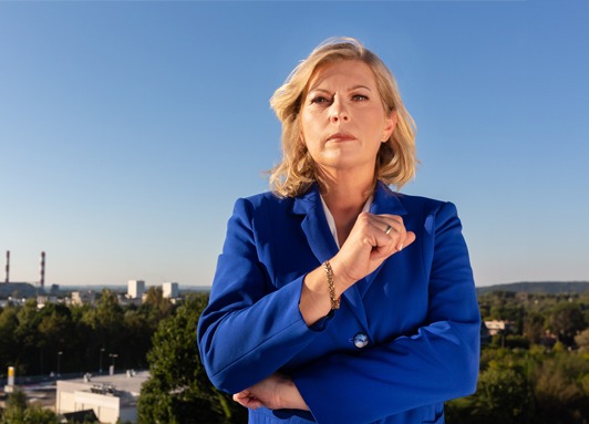 Anna Wąsowicz stojąca pewnie na tle panoramy Skawiny, symbolizująca jej determinację w zamiarze kandydowania na burmistrza.